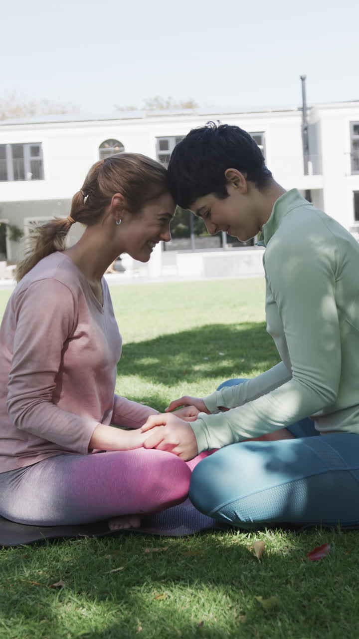 una feliz pareja de lesbianas caucásicas practicando yoga en un jardín soleado, en cámara lenta