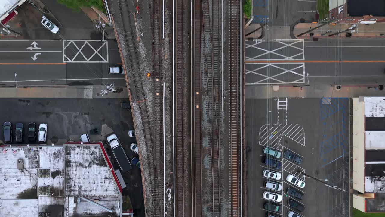 A top down, aerial view of the Long Island Railroad train tracks running through an industrial area on Long Island on a cloudy day. The camera is tilted straight down and slowly dolly in.