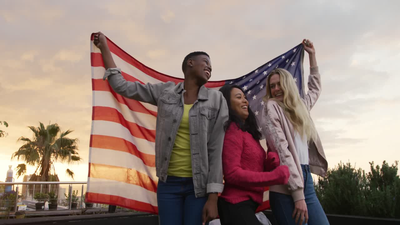 Giovani donne che ballano e tengono la bandiera americana su un tetto