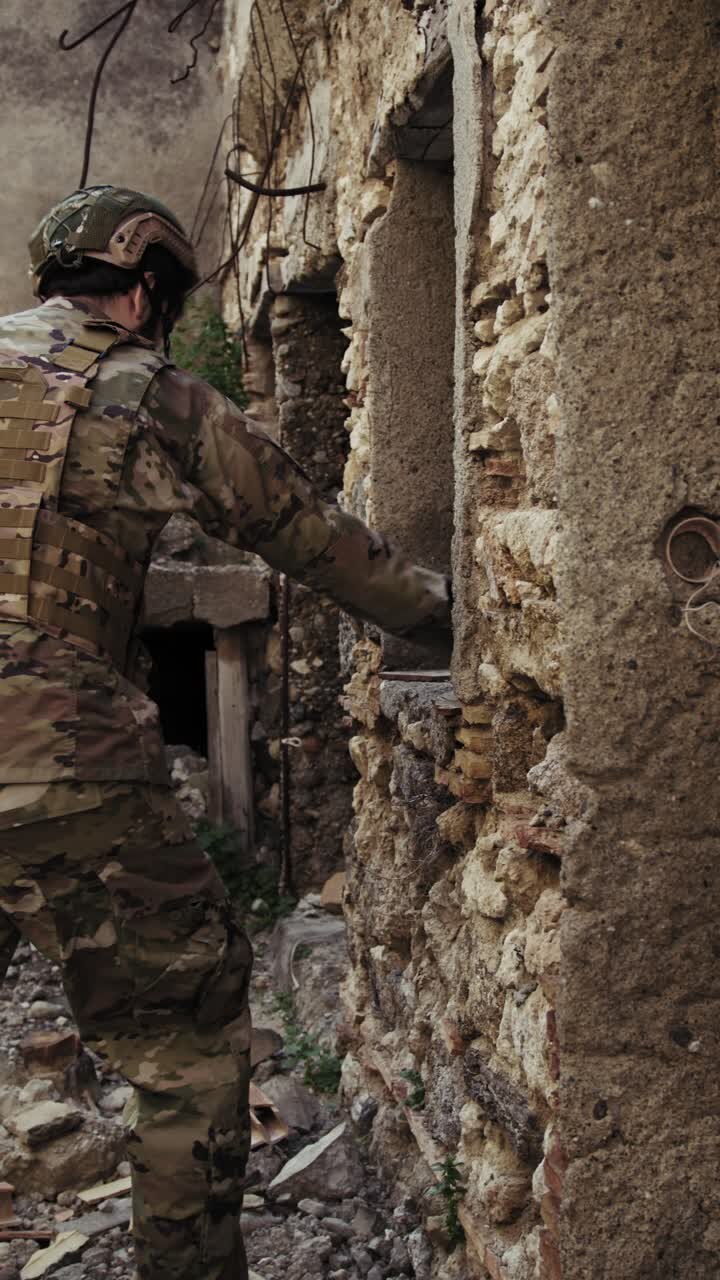 Soldato in uniforme che ispeziona i muri delle case distrutte in città