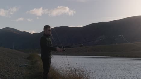 young male fisher casting out rod into hydro canal in front of mountainous scenery