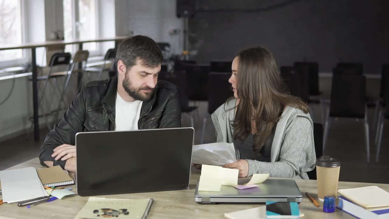 Businesswoman arguing with her male colleague in the office, closing his notebook and throwing papers. Angry female worker