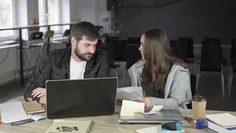 businesswoman arguing with her male colleague in the office, closing his notebook and throwing papers. angry female worker