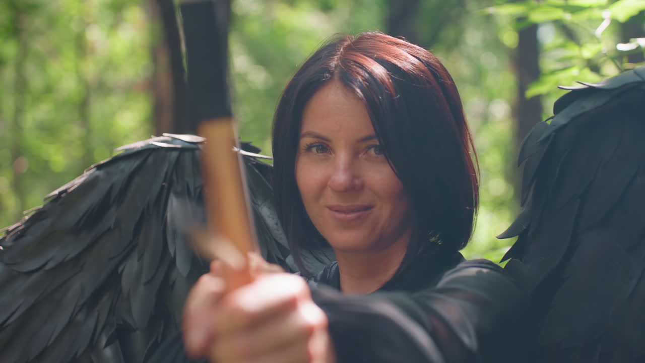 Beloved of Eros with black wings aims bow in forest as sunlight glows behind her, eyes steady with strength and grace, mystical atmosphere blending divine power