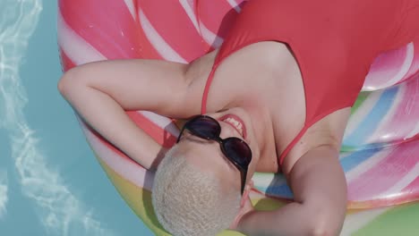 happy biracial woman with sunglasses lying on inflatable in swimming pool in slow motion