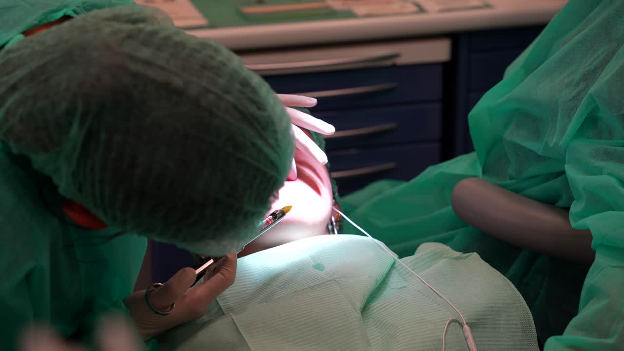 Medium shot of dentist using syringe to apply anesthesia to patient's lower jaw and continues to upper part