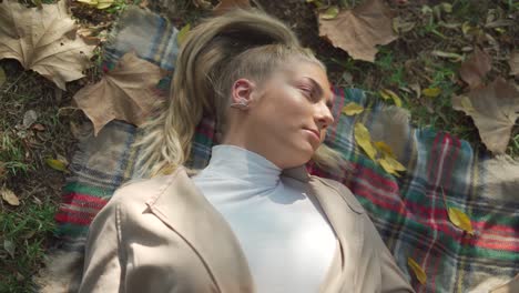 smiling female lying on plaid with dry leaf in park