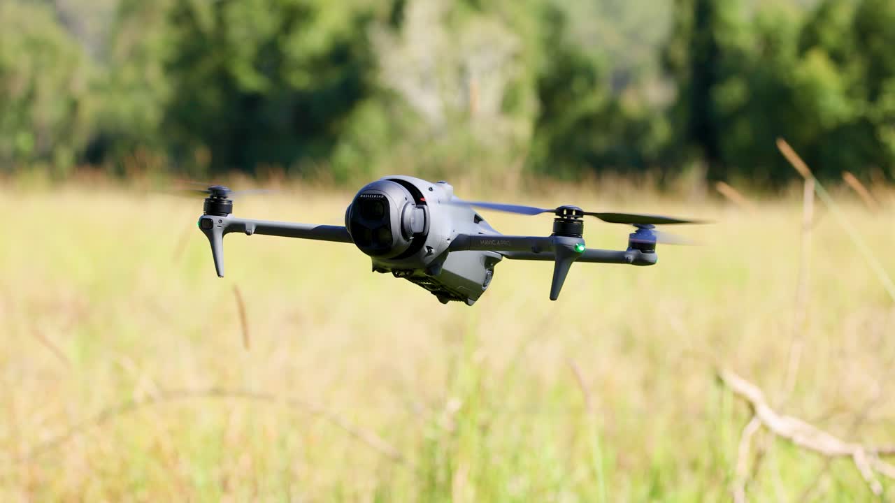 A drone hovers steadily over a grassy field in Gold Coast, Australia, under bright daylight, showcasing smooth flight and stability