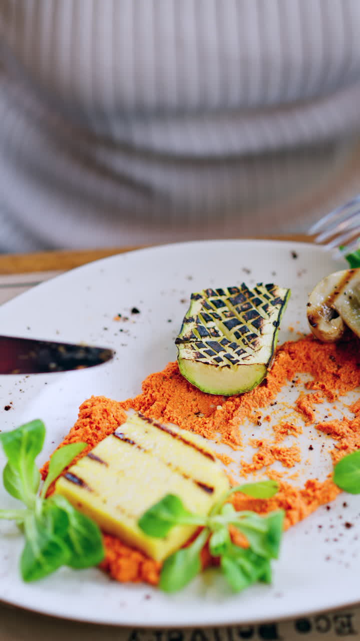 Woman eating grilled zucchini with mushrooms, polenta and hummus. Vertical
