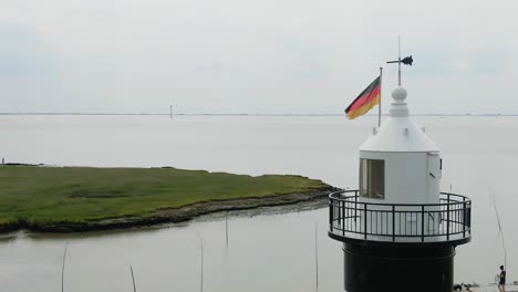 "In-the-background-of-the-North-Sea,-a-lighthouse-can-be-seen-with-a-German-flag-waving