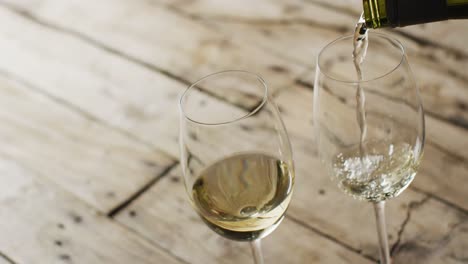 White-wine-pouring-into-glasses-over-wooden-surface-with-copy-space