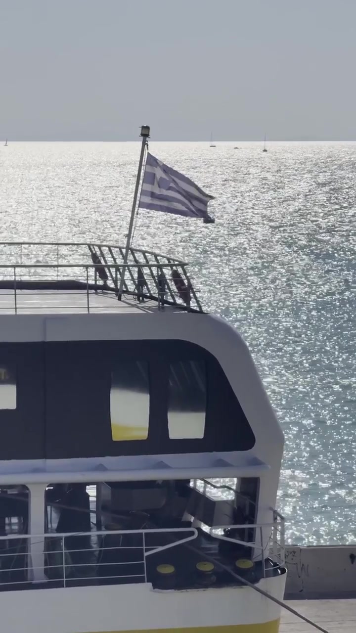 Nærbillede af sommerudsigt over en græsk færge og et viftende nationalflag med vand i baggrunden