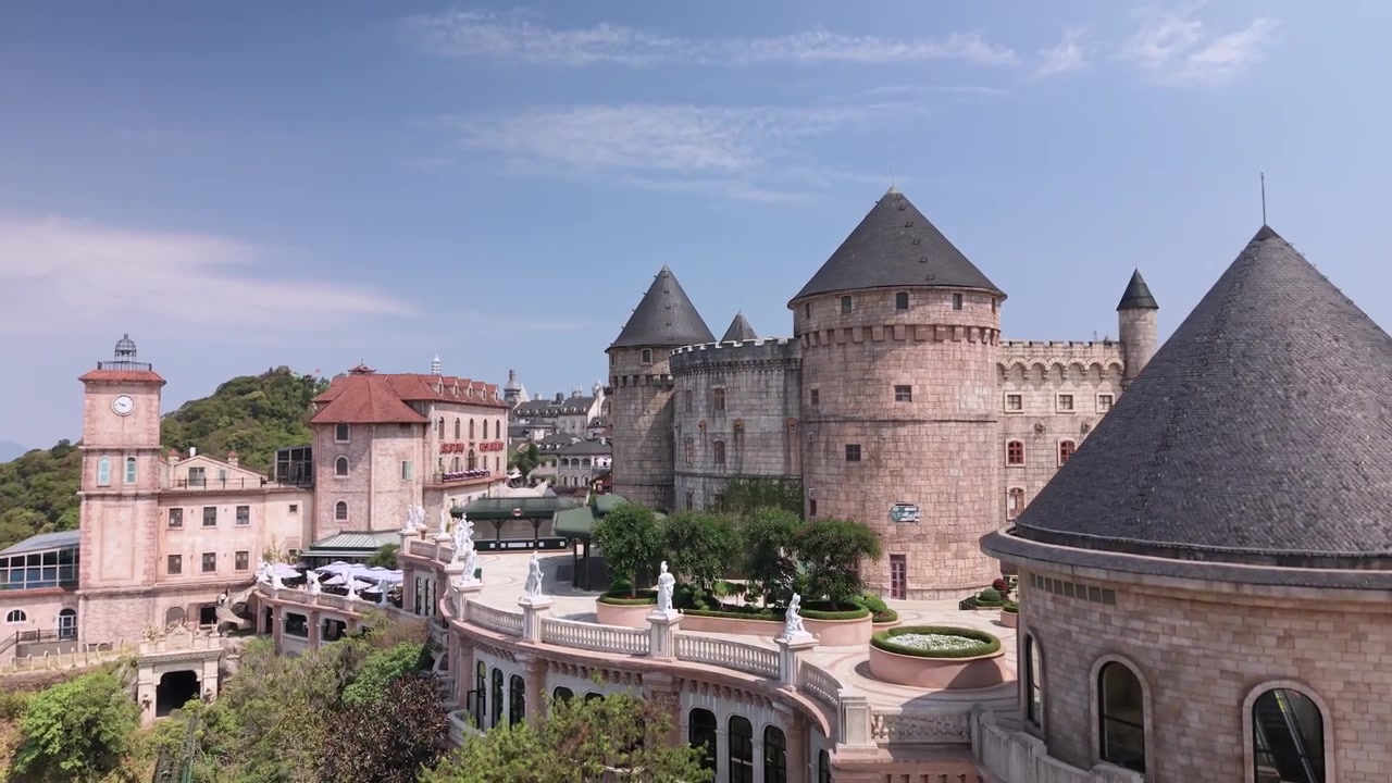 Le riprese aeree con drone catturano il complesso del castello Ba Na Hills SunWorld circondato da una vegetazione lussureggiante e montagne distanti sotto un cielo sereno in Vietnam.