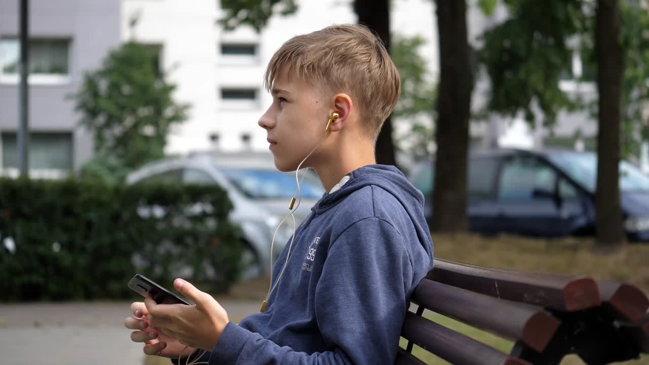 벤치에 앉아서 듣고 즐기고, 머리를 흔들며 음악을 연주하는 어린 소년