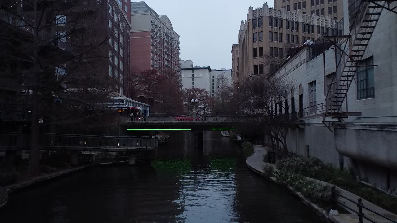 A drone soars over a winding river, reflecting city lights as bridges and skyscrapers frame the urban landscape.