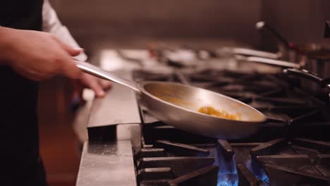 cook shakes the silver pan with pasta back and forth while the pasta cooks on the fire