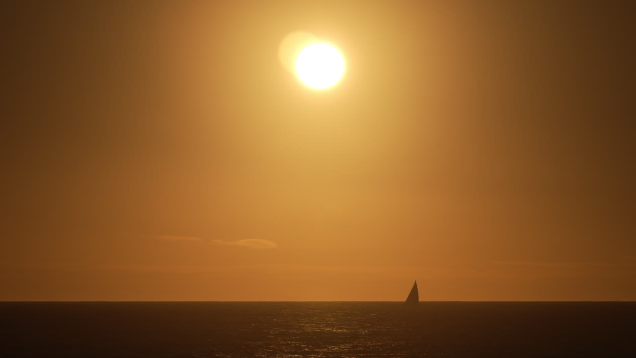 황금빛 해가 지는 동안 바다의 지평선에서 항해하는 요트