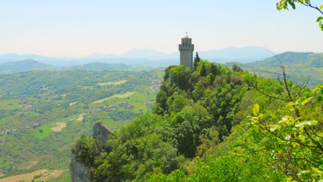 shot of montale tower on the hill top through the trees in san marino, italy on a bright sunny day