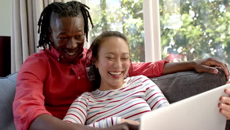 happy diverse couple relaxing on couch using laptop in living room, slow motion