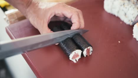 A-professional-chef-cuts-a-roll-of-sushi-with-tuna-into-pieces,-making-tuna-maki-rolls,-traditional-Japanese-cuisine