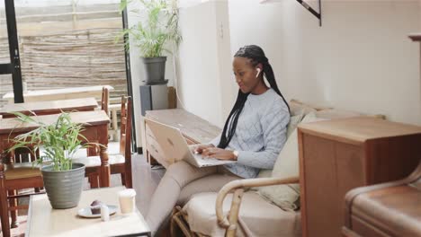 happy african american woman using laptop sitting in coffee shop, slow motion