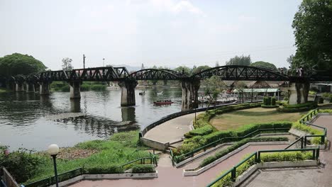 hd wide shot of bridge over the river kwai in kanchanaburi, thailand with boats under the historical structure