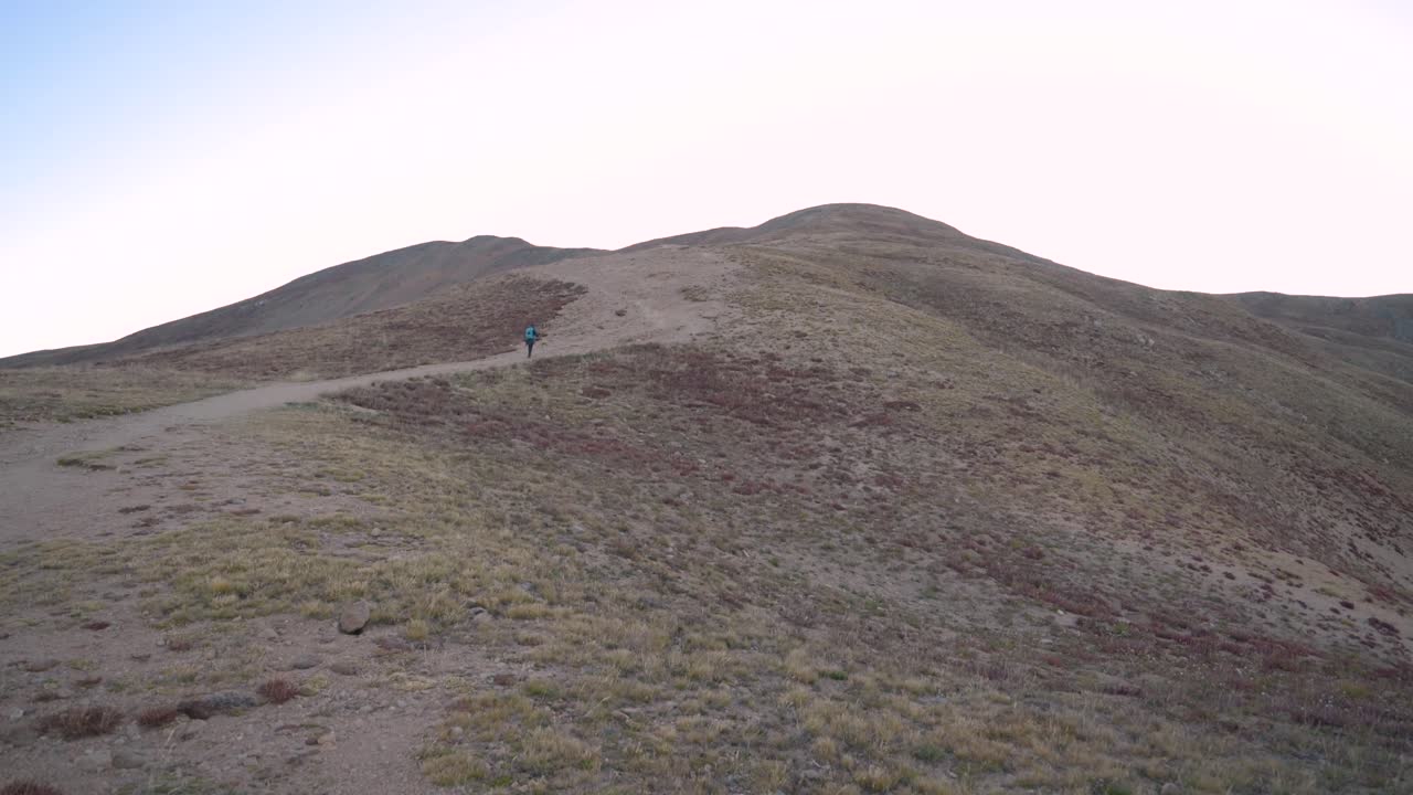 mujer caminando sola por un sendero de montaña empinado antes del amanecer en un día sin nubes, inclinación de mano