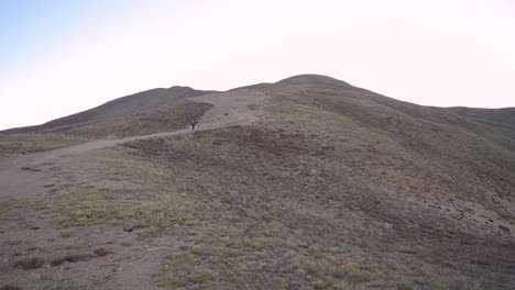 female hiking alone up steep mountain trail before sunrise on a cloudless day, tilt handheld