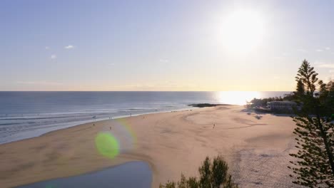 Pocas-Personas-Caminando-En-Las-Rocas-De-Pargo-Durante-El-Amanecer---Luz-Solar-Brillante-Sobre-El-Océano-En-Calma---Bahía-Del-Arco-Iris-En-La-Costa-Dorada,-Queensland,-Australia