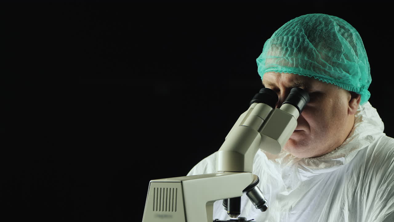 técnico de laboratorio masculino mira al microscopio contra fondo negro