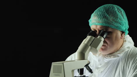 Male-lab-technician-looks-into-microscope-against-black-background