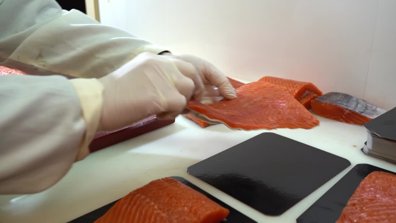 포장하기 전에 종이 접시에 신선한 훈제 연어 조각을 넣는 흰색 작업복을 입은 사람