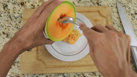Hands of a man removing seeds of melon using a spoon