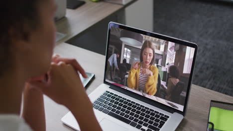 african american businesswoman sitting at desk using laptop having video call with female colleague