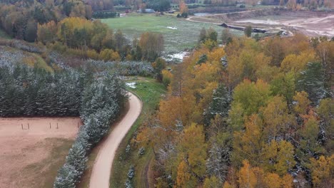 a drone flies over ogres zilie kalni in latvia, revealing the quarry parking area bordered by autumn forests with snow-dusted, colorful trees for a vibrant seasonal view