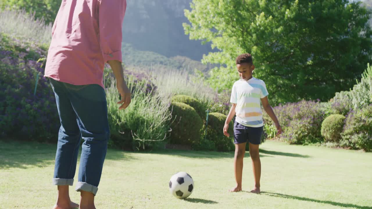 padre e hijo afroamericanos felices jugando al fútbol en el jardín, en cámara lenta