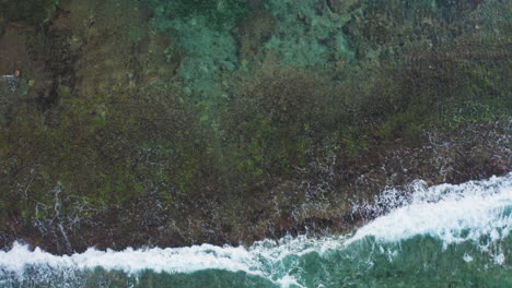 pushing drone up and camera down bird's eye perspective to film amazing waves crushing on beach rocks in bali indonesia