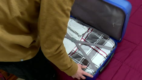 person packing a blue suitcase on a bed