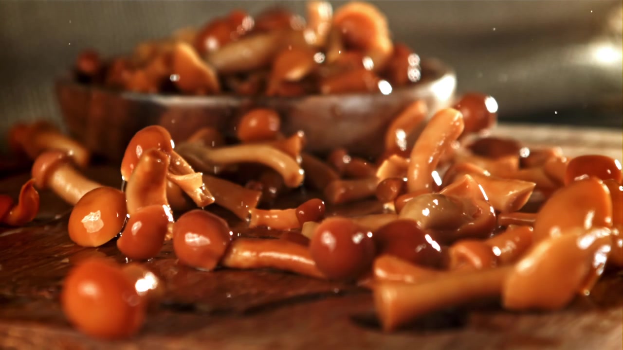 Funghi sott'aceto che cadono su un tagliere di legno bagnato al rallentatore