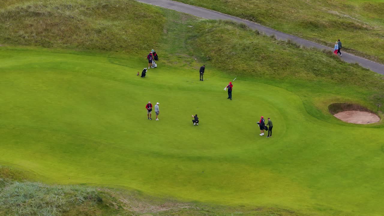 Drone captures group of golfers putting on green, overcast lighting, wide aerial perspective, Carnoustie