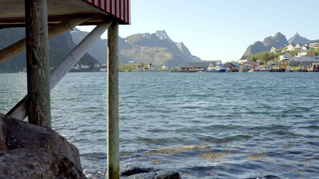 Looking across water to buildings of Reine, Lofoten, Norway from below a rorbu, or traditional fisherman’s hut