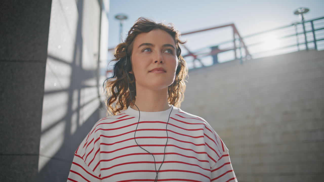 niña despreocupada escuchando música con auriculares en la calle soleada retrato de cerca.