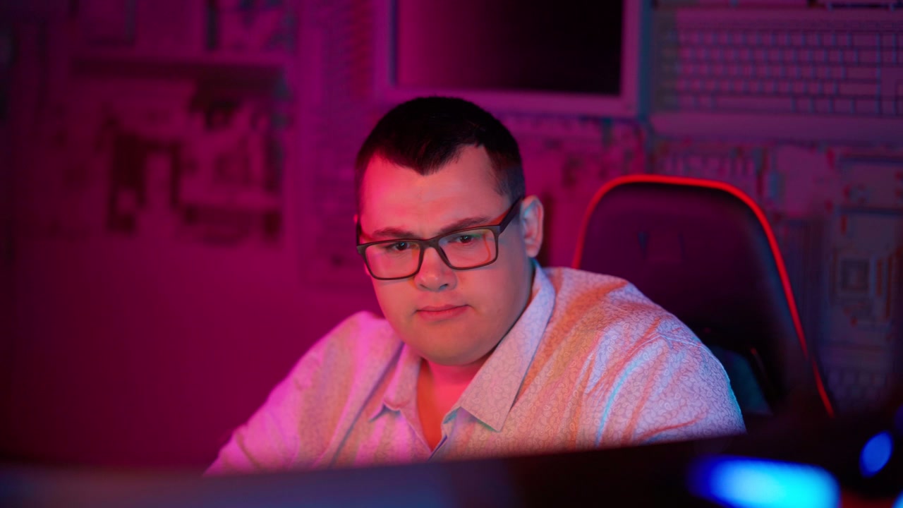 Young Man in Glasses Focused on Computer Screen with Neon Lighting