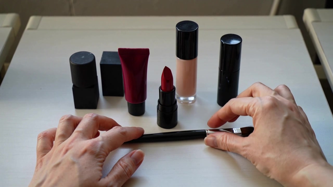 Entering hands placing red lipstick upright on pale table by window, aligning brush for display