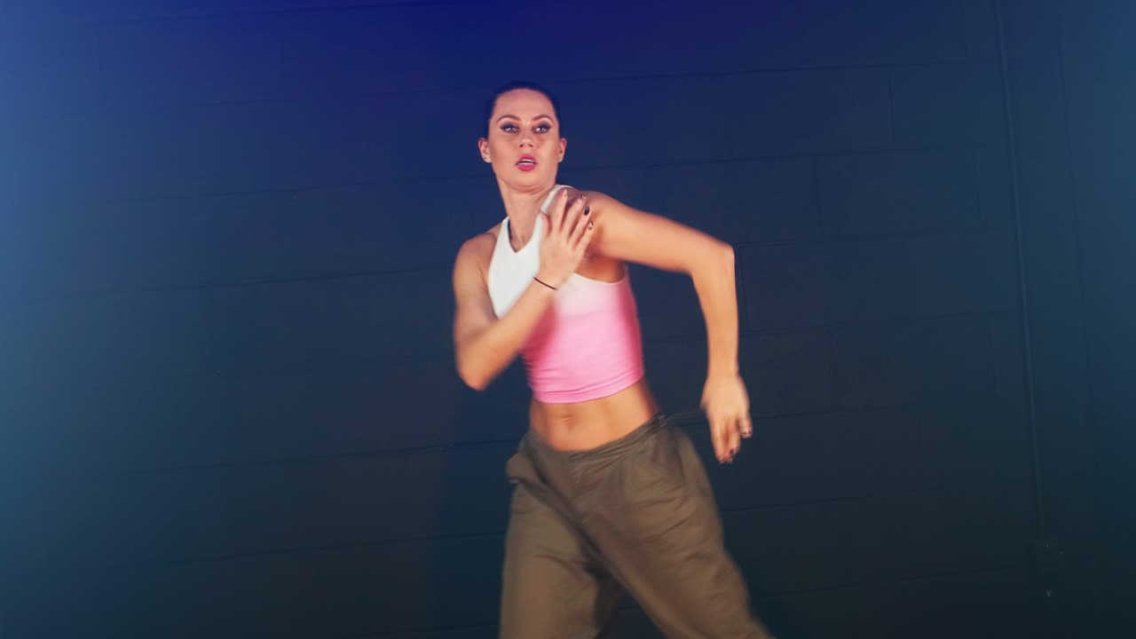 atractiva morena blanca bailando sexy en una habitación oscura con una camiseta rosa blanca