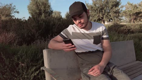 a man is sitting on a bench and looking at his cell phone