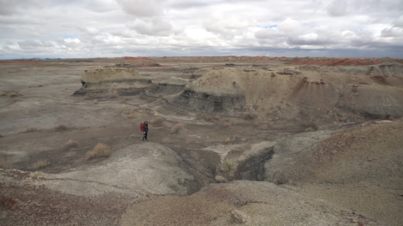Woman With Backpack Walking in Barren Desert Landscape of Bisti De-Na-Zin Wilderness, New Mexico USA, Full Frame, Panorama