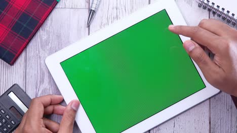 person using a tablet with a green screen on a desk