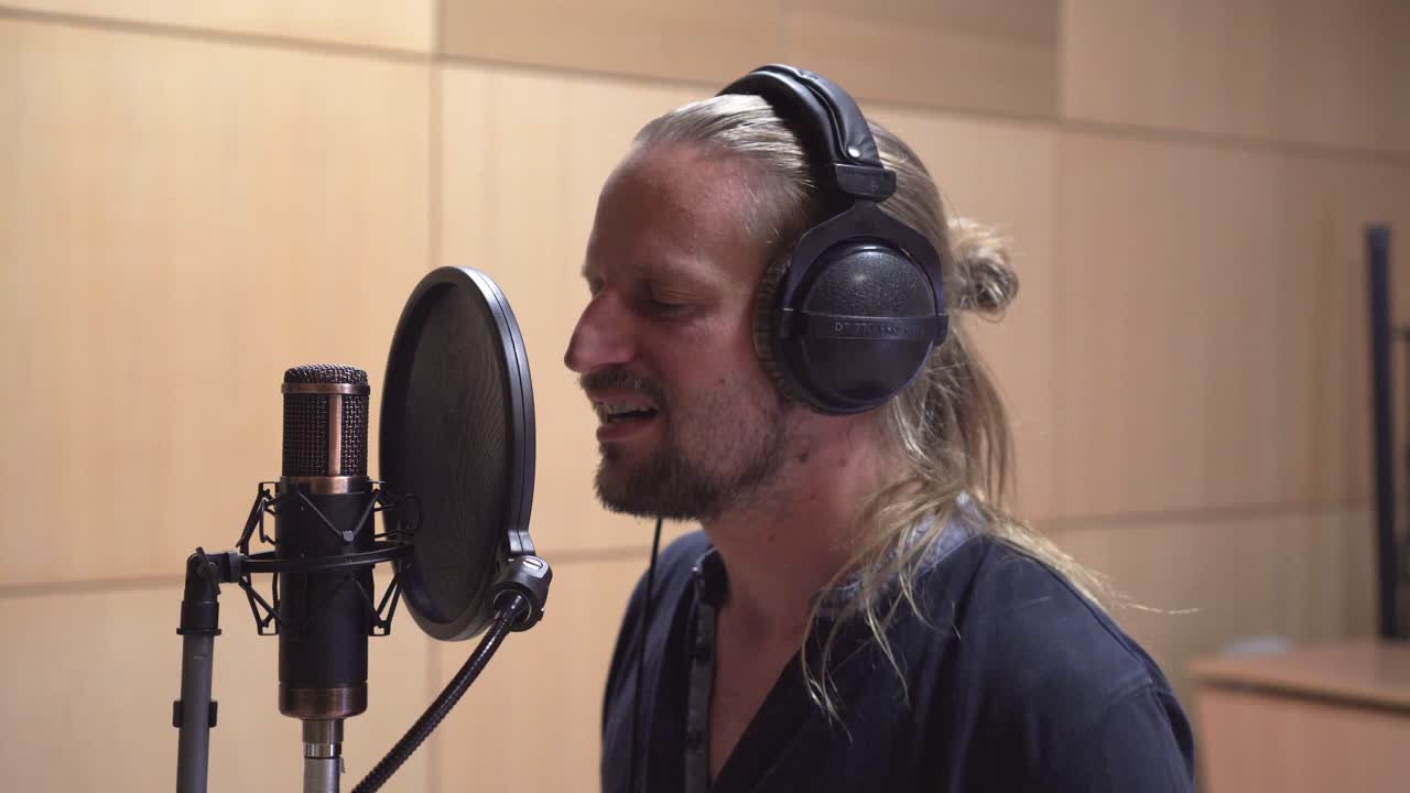 Male singer singing in recording studio, side close up, head and face