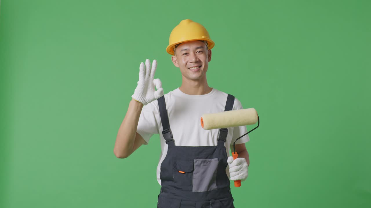 Asian Man Painter Wearing Safety Helmet Smiling And Showing Okay Gesture To Camera While Standing In The Green Screen Background Studio
